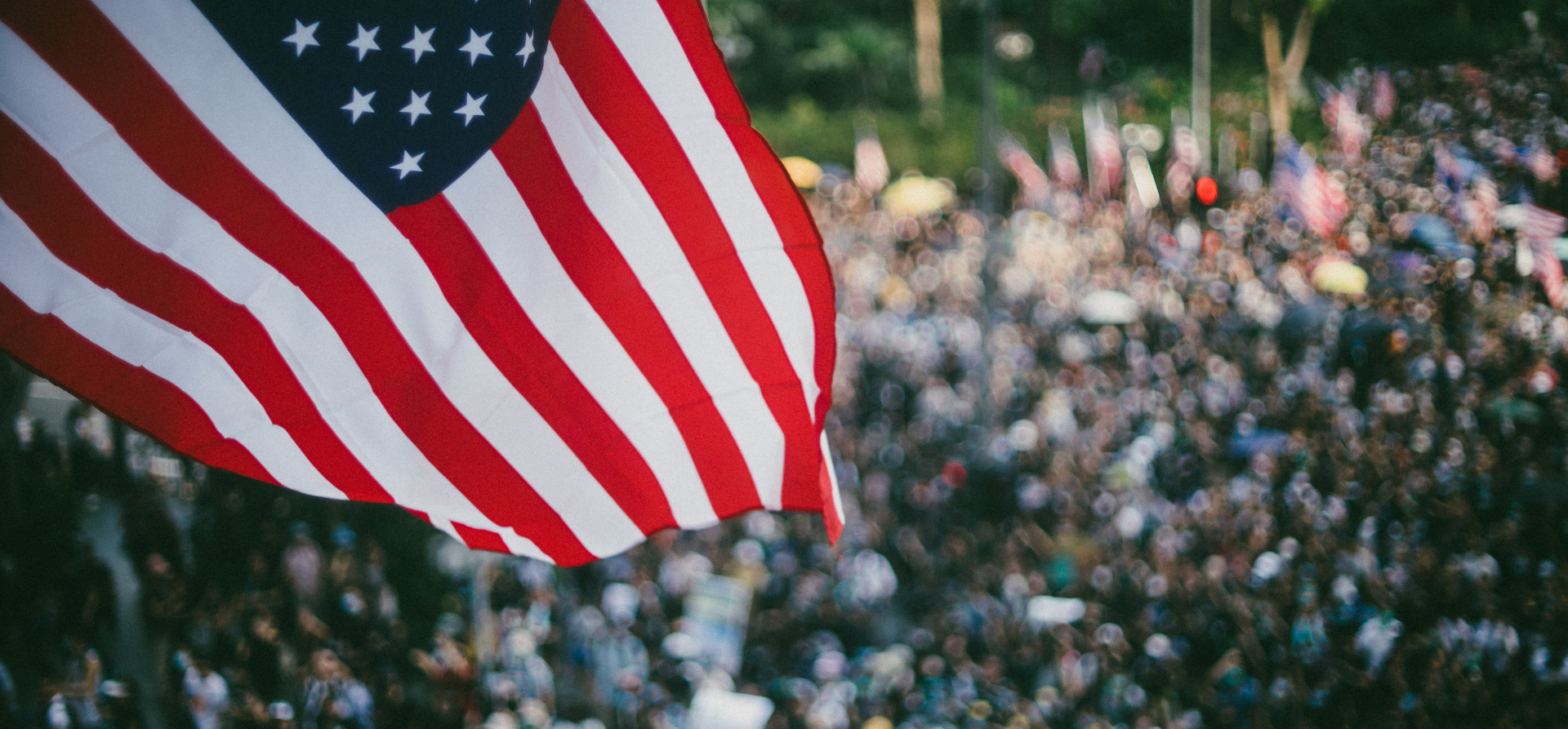 Aerial photo of US flag above out-of-focus crowd.
